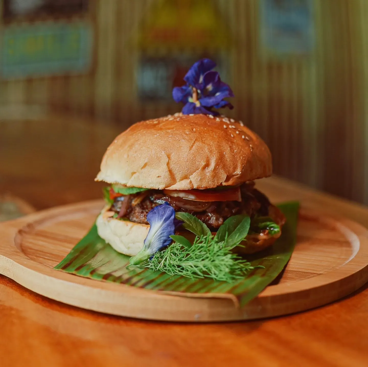 Signature burger topped with edible flowers on a bamboo plate at Patrick's on the Beach restaurant