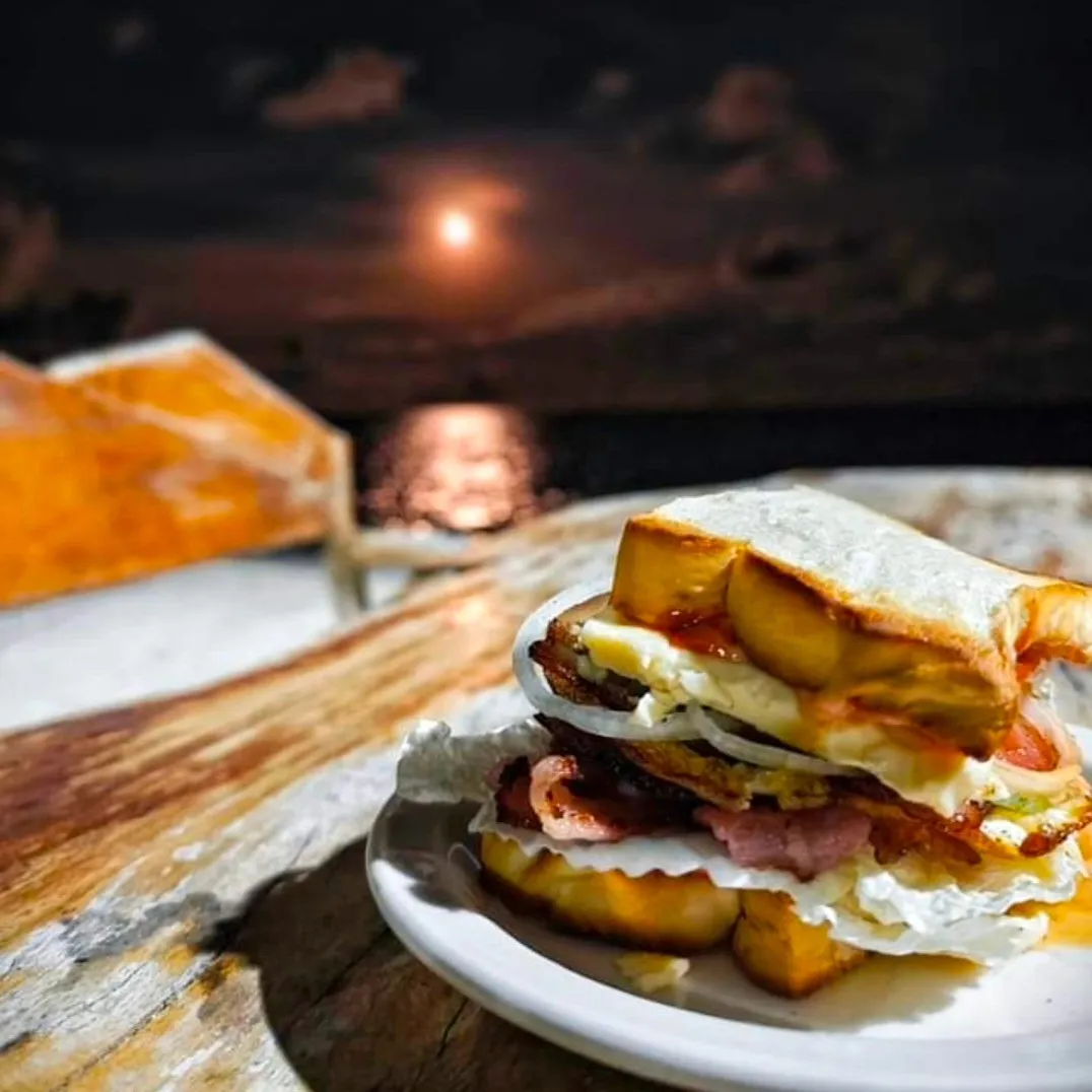 Bacon and egg sandwich on a plate with the moon rising over the sea behind, at Patrick's beachfront tables in General Luna