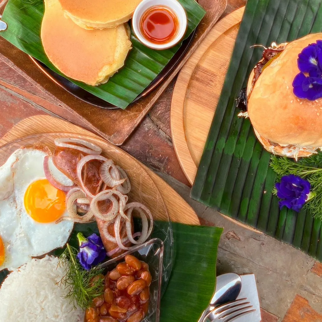 Breakfast spread served on banana leaves at the beachfront restaurant of Patrick's on the Beach, Siargao: pancakes, a burger, eggs and rice