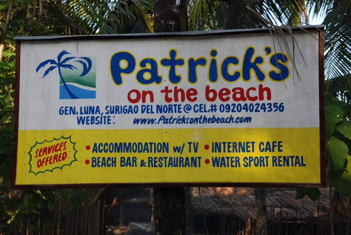 The original hand-painted Patrick's on the Beach sign in General Luna, framed by palm fronds