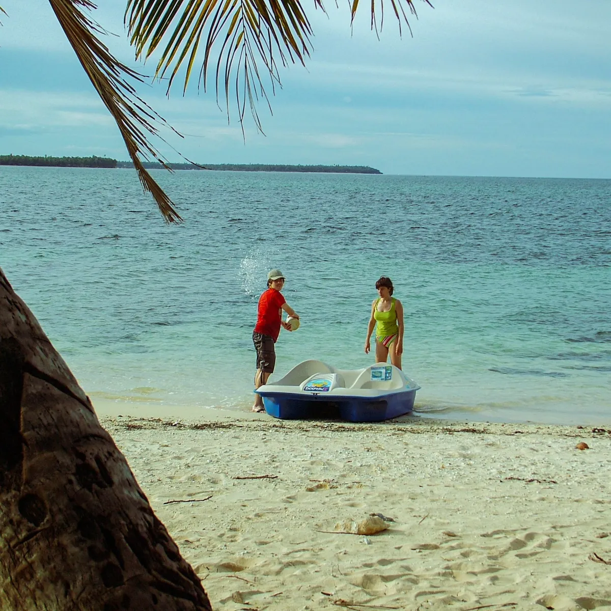 Two guests beside a paddle boat on a white-sand island beach near Siargao