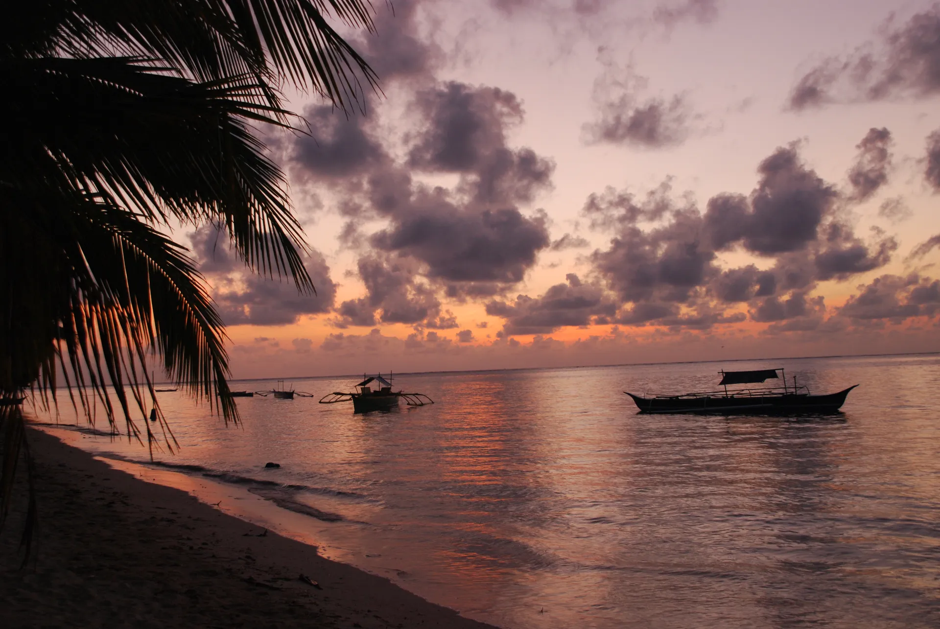 Outrigger boats resting on calm water at sunset off the beach in General Luna, Siargao