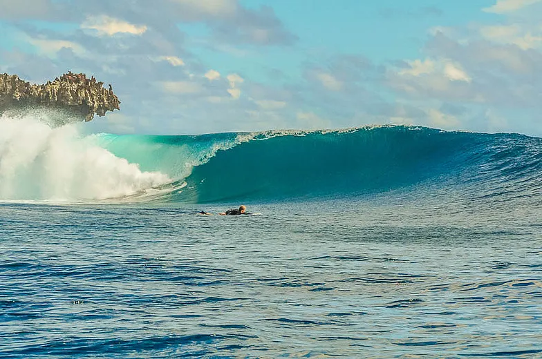 Surfer paddling toward a glassy wave breaking off Rock Island, Siargao