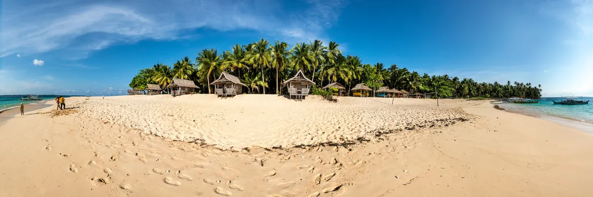 Panorama of Daku Island's white-sand beach, palm trees and outrigger boats near Siargao