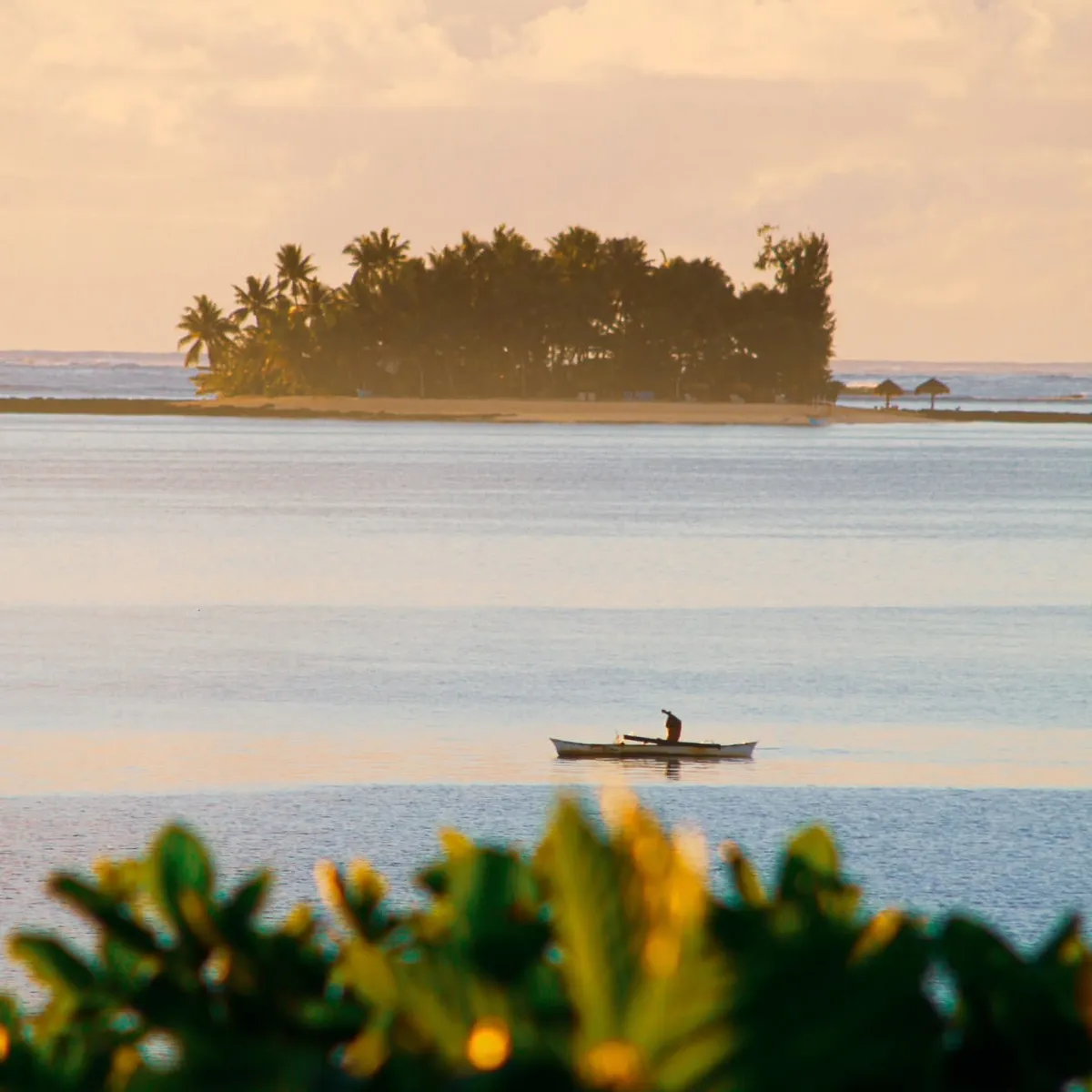 Kayaker paddling toward a small palm-covered island off General Luna at golden hour